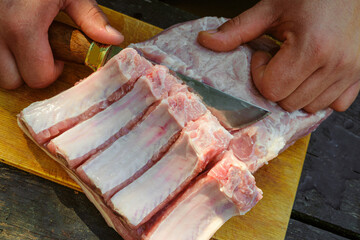 Cutting fresh meat with a knife on a wooden cutting board. Pork ribs with meat.