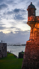 Old Sentry Box on Curtain Wall at National park Castillo San Felipe del Morro Fortress lighted up at at dusk with Isla de Cabras and tourists in background in old San Juan, Puerto Rico, a UNESCO site