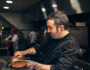 Chef, sauce and mixing in kitchen with food, restaurant and preparation process in hospitality service. Professional meal prep, man or cooking gravy dish at diner for order, soup or culinary industry