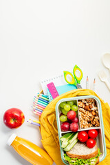 Healthy school lunchbox with fruits, veggies, and walnuts and school stationery on white background