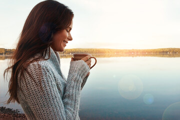 Outdoor, lake and coffee to enjoy with woman, nature or sunrise in morning, thinking and break for vacation. Travel, happy and girl with tea, smile and trip in autumn, peace or countryside in Finland