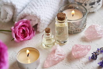 Two bottles of aromatherapy essential oil with lavender and rose de Mai flowers, rose quartz stones and white spa towels