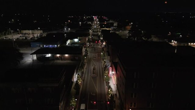 The main street of an old downtown section of a small city in the Midwest USA is shown from an aerial flyover view at night.