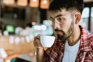 Portrait of a bearded Asian man wearing glasses drinking coffee in the cafe. close-up