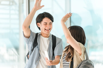 スマホを見て喜んでハイタッチする学生・大学生の男女