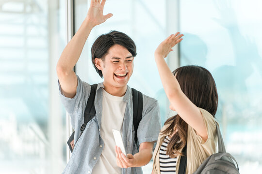 スマホを見て喜んでハイタッチする学生・大学生の男女
