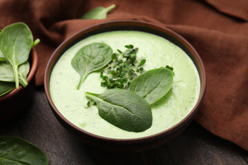 Delicious spinach cream soup with fresh leaves and microgreens in bowl on wooden table