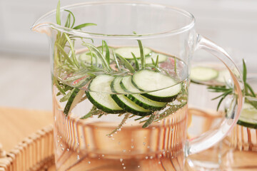 Refreshing cucumber water with rosemary in jug on blurred background, closeup