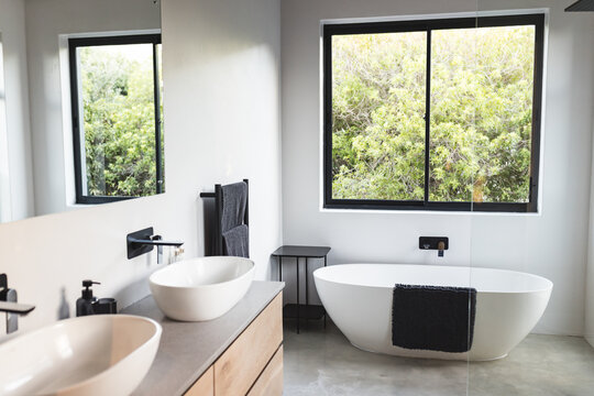 Modern bathroom with freestanding bathtub, double sinks, and large window, copy space