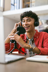 Recording podcast, smiling young man using microphone and laptop at home studio