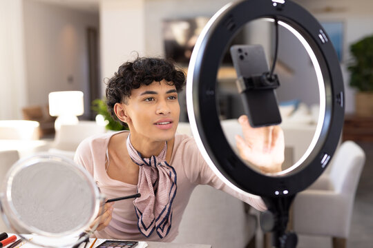 Applying makeup, transgender transgender woman using smartphone and ring light at home - Powered by Adobe