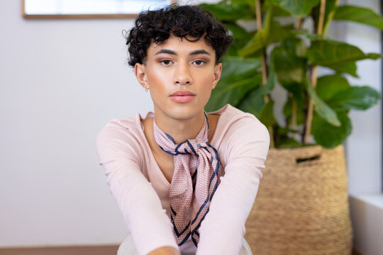 Sitting indoors, transgender transgender woman posing confidently with plant in background