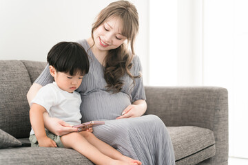 スマホを見る子供と子守をする妊娠中のママ・母親・妊婦
