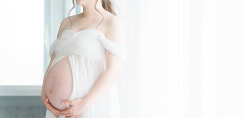 家のカーテンの前でマタニティフォトの撮影をする妊婦のアジア人女性
