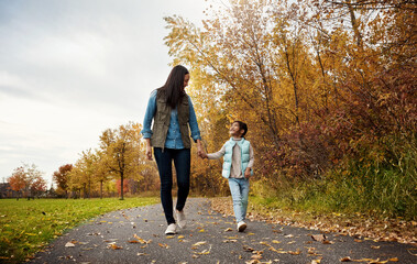 Happy mother, walking and holding hands with child for bonding, outdoor adventure or journey in nature. Mom strolling with daughter, kid or little girl on sidewalk in autumn season at park together