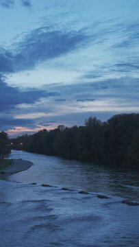 Munich at dramatic dusk sunset. View of Isar river, trees and St Maximilian church from Reichenbach Bridge in Autumn. Munchen, Bavaria, Germany. Camera horizontal pan