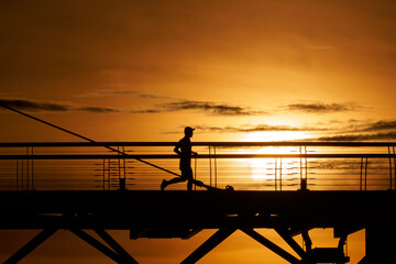Silhouette man running across the bridge against sunset.