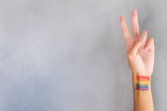 Hand showing peace sign with rainbow flag painted on wrist, expressing LGBTQ+ pride