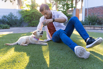 Playing with puppy, man sitting on grass in backyard enjoying sunny day