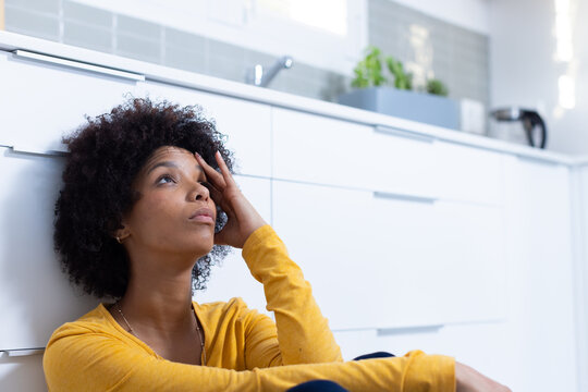 Sitting on kitchen floor, woman looking thoughtful and touching her forehead