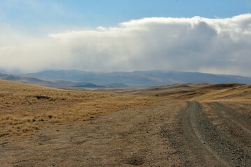 A winding field road rises to the top of the hill towards thick clouds in the autumn steppe.