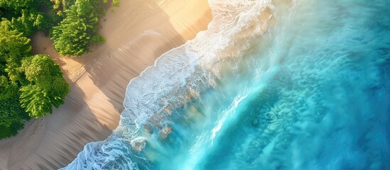 Aerial view of turquoise ocean waves crashing on sandy beach with lush green trees. Tropical paradise, summer vacation, travel, and nature concept.