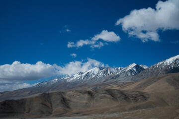 The view is breathtaking from the green hills to the huge snow-capped mountains beneath the clouds in the blue sky. Beautiful scenery with a large snow peak in the middle.