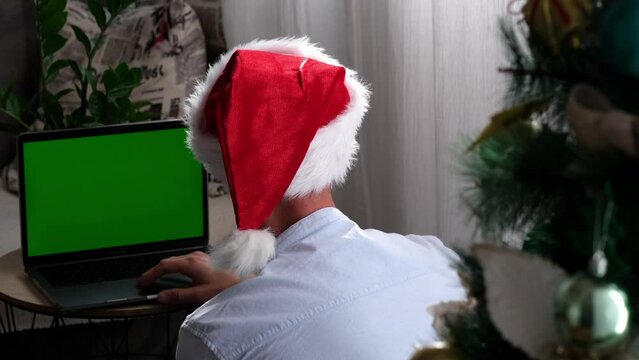 young man in Santa hat sitting at green screen laptop back view of merry christmas and new year