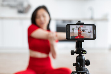 Woman in red outfit recording fitness video on smartphone during workout session in bright room. Concept of fitness, health, social media content creation, and online coaching.