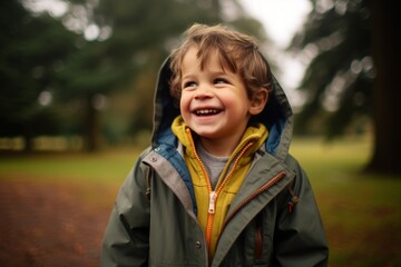 Fototapeta premium Portrait of a smiling little boy in a raincoat in the park