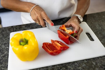 Woman with red manicure cutting red and yellow peppers on a chopping board