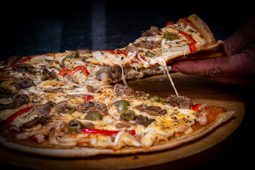 Close-up of a hand taking a slice of vegetarian pizza with onions, bell pepper, and vegetables on a wooden board.