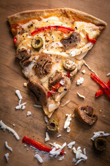 Close-up of a hand taking a slice of vegetarian pizza with onions, bell pepper, and vegetables on a wooden board.