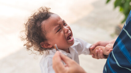 A young asian boy with curly hair crying and throwing a tantrum after not getting his toy back.