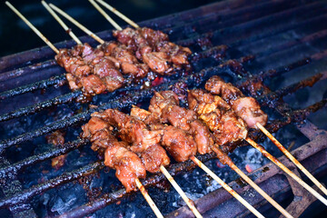 Satay is being grilled on a grill using coals and emitting smoke