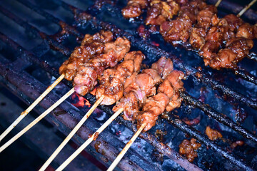 Satay is being grilled on a grill using coals and emitting smoke