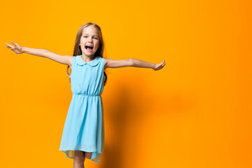 Joyful little girl in blue dress leaping with happiness against vibrant orange background