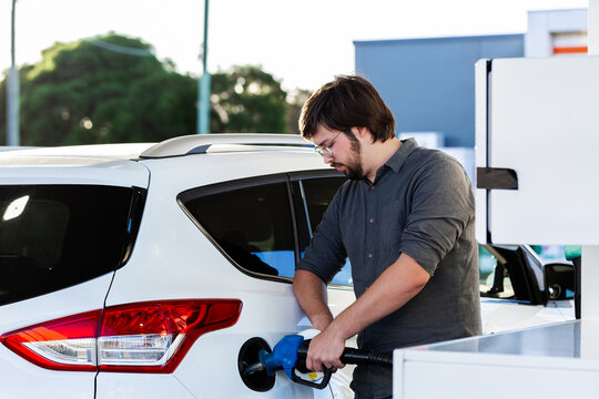 young man in his twenties filling family car with petrol at servo station bowser