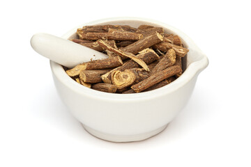 Close-up of Dry Organic Liquorice or Mulethi (Glycyrrhiza glabra), in white ceramic mortar and pestle, isolated on a white background.