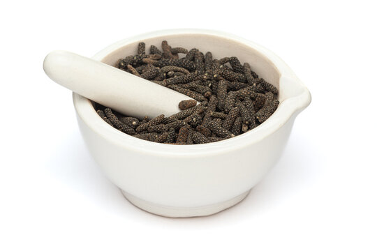 Close-up of Dry Organic Long pepper (Piper longum) fruit, in white ceramic mortar and pestle, isolated on a white background.