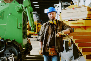 Medium long shot of confident Caucasian man with beard on face standing at workplace in modern bulldozer production factory