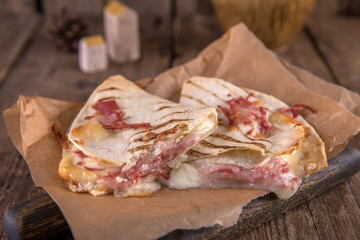 Quesadilla with cheese and ham on craft paper on a wooden table