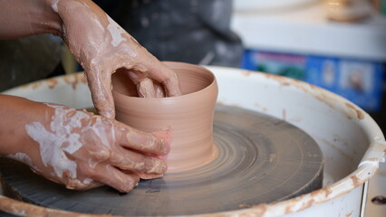 Smoothing clay pottery with sponge at throwing wheel.