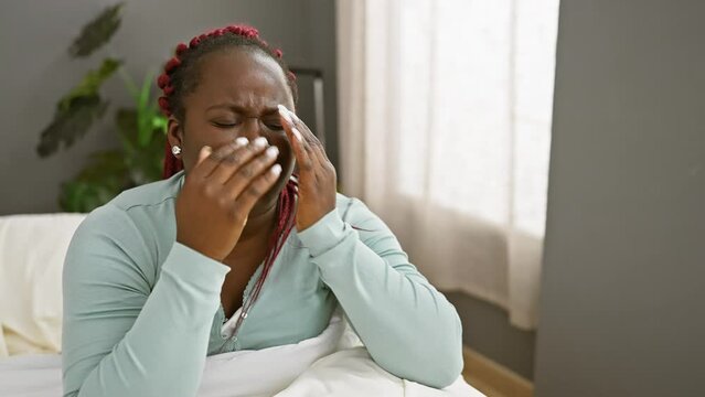 A distraught african american woman with braids sitting in a rehab clinic room, portraying a scene of healthcare and emotional distress.
