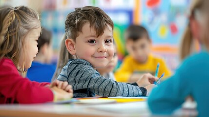 Obraz premium A young boy smiles at the camera while sitting at a table with other children in a classroom.
