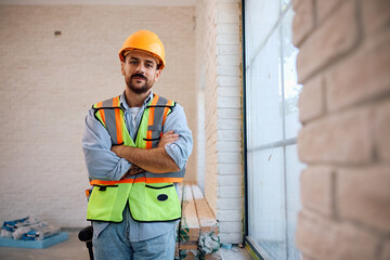 Manual worker with arms crossed at construction site looking at camera.