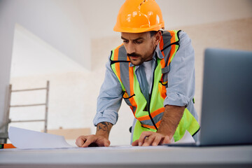 Construction site worker analyzing housing plans during home renovation project.