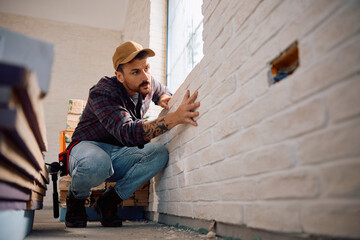 Manual worker examining  wall at construction site.