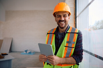Happy manual worker working on touchpad at construction site and looking at camera.