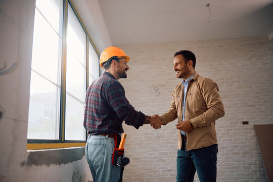 Happy man shaking hands with construction site worker at his renovating home.